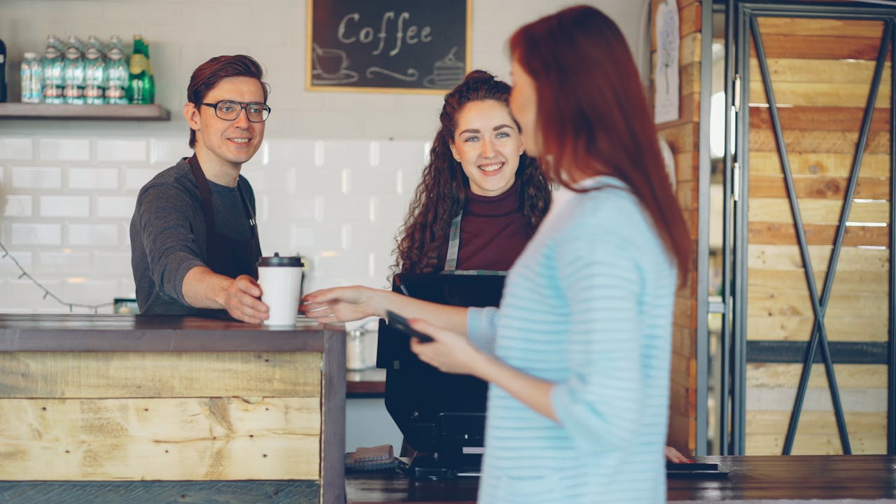 Barista hands coffee to a customer in a cozy café setting.